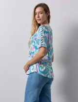 Remera de algodón estampado con diseño paisley en tonos celeste, rosa y amarillo. Tiene cuello redondo y mangas cortas con detalle de entrelazado y aberturas en los hombros.
