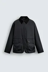 Parka de corte relajado en color negro, confeccionada en tejido de algodón con interior ligeramente acolchado. Presenta cuello de solapa en pana, cierre frontal con cremallera y bolsillos delanteros tipo plastrón con solapa y botones a presión.