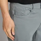 Pantalón chino de hombre, color gris verdoso, corte slim y tiro medio. Presenta cinco bolsillos y puños doblados.
