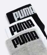 Pack de tres pares de medias deportivas Puma de caña corta, confeccionadas en tejido de algodón con textura. Incluye un par negro, uno blanco y uno gris, cada uno con el logo de la marca en el talón y el nombre en la parte superior.