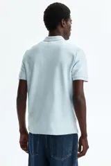 Remera polo H&M de manga corta color celeste, confeccionada en punto jacquard de mezcla de algodón, con cuello clásico y tapeta con dos botones.
