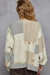 Cardigan de punto con diseño patchwork en bloques de color gris, blanco y beige, de manga larga abullonada, cuello en V y cierre frontal con botones.