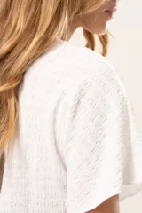 Blusa blanca de textura arrugada con cuello redondo y mangas cortas, de corte recto y estilo casual.