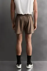 Pantalón corto deportivo color marrón oliva, confeccionado en tejido técnico ligero y elástico, con forro interior. Presenta cintura elástica ajustable con cordón, bolsillos frontales, bolsillo de seguridad trasero con cierre y aberturas laterales en el bajo.