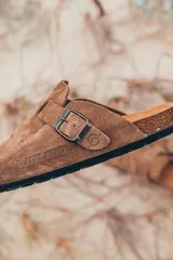 Zueco marrón de gamuza con hebilla metálica ajustable y suela de corcho. El logo "Glassy Waves" está grabado en el lateral.