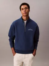 Buzo Calvin Klein de color azul marino, confeccionado en mezcla de algodón y poliéster. Cuenta con cuello alto, cierre de media cremallera y manga larga con hombros caídos. Presenta puños y dobladillo acanalados, y el logo de la marca bordado en punto de cadeneta en el pecho.