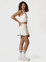 Falda short deportiva color blanco con borde inferior en contraste negro. Presenta un diseño de tiro alto con falda acampanada y short integrado con bolsillo oculto.