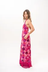 Vestido largo fucsia con estampado abstracto en tonos rosados y morados, cuello halter cruzado y flecos largos en el dobladillo inferior.