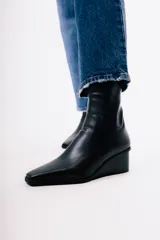 Bota de caña media en cuero negro, con diseño de punta cuadrada y taco cuña integrado.