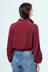 Camisa bordó de manga larga abullonada, con costuras en contraste color blanco, cuello camisero y cierre frontal de botones.