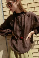 Blusa de cuello subido y manga larga abullonada con puños ajustados. Presenta un diseño semitransparente con textura arrugada y cierre frontal con botones a tono.