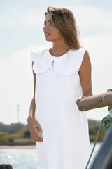 Vestido corto de color blanco, sin mangas, con cuello estilo Peter Pan con volados y cierre frontal.