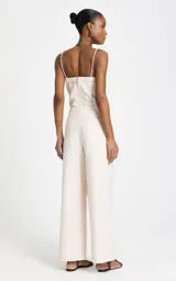 Pantalón sastrero de lino y algodón color beige, de tiro alto y corte ancho (wide leg). Presenta sutiles pliegues frontales, trabillas con apliques metálicos dorados en la cintura y bolsillos laterales.