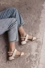 Sandalia de cuero color beige claro (off white) con taco ancho y tiras finas ajustables con hebilla metálica dorada en el tobillo.