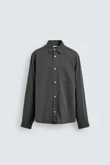 Camisa de corte relajado confeccionada en una mezcla de lyocell y algodón con efecto lavado. Presenta cuello solapa, manga larga con puños abotonados, bolsillo de plastrón en el pecho y cierre frontal con botones.