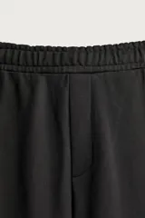 Pantalón jogger de corte relajado y pernera ancha, confeccionado en tejido de algodón con interior perchado. Cuenta con cintura elástica ajustable mediante cordón interior, bolsillos laterales y un bolsillo trasero de plastrón.