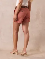 Short de jean azul oscuro con tiro medio, cierre frontal con botón y pasadores para cinturón. Incluye un cinturón trenzado de cuero sintético color marrón con hebilla circular metálica.