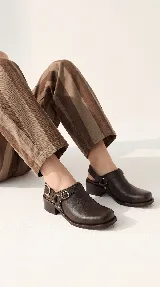 Zueco de cuero marrón oscuro, con diseño cerrado en la parte delantera, tira ajustable en el talón con hebilla metálica y taco bajo cuadrado.