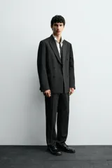 Pantalón de vestir negro con pliegues frontales, corte regular fit, bolsillos laterales y traseros de doble vivo con botón. Cierre frontal cruzado con cremallera y gancho metálico.