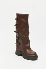 Bota de caña alta estilo biker, color negro, con plataforma robusta y suela dentada. Presenta múltiples tiras laterales con hebillas metálicas ajustables.