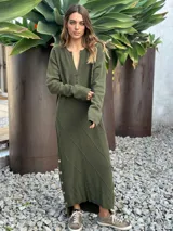 Vestido midi de punto color verde oliva, con cuello en V, manga larga y diseño con textura de rombos. Presenta una abertura lateral con botones decorativos y un corte asimétrico en el ruedo.