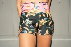 Short deportivo tiro alto con estampado de flores y hojas en tonos verde, naranja, amarillo y azul sobre fondo negro.