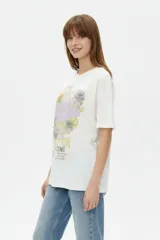 Remera de algodón color marfil, de corte holgado y mangas cortas, con cuello redondo y estampado frontal de diseño inspirado en la música con texto "The Endless County Keep On Rocking" y detalles de girasoles.