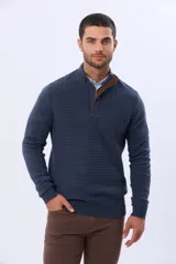 Buzo de punto color beige, con cuello alto y cierre frontal con cremallera y solapa de gamuza con botón. Presenta un tejido texturizado en el cuerpo y mangas lisas.