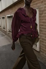 Blusa de color bordó con escote en V profundo adornado con volantes, mangas largas con puños y detalle de peplum en el ruedo. Cuenta con cierre frontal de botones forrados en la misma tela.