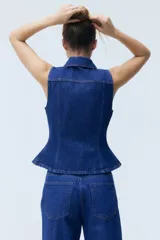 Chaleco de denim azul rígido de algodón, con cuello camisero, cierre frontal de botones metálicos, bolsillos con solapa en el pecho y detalle de peplum en la parte inferior.