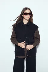 Chaleco de jean negro de corte oversized, con cuello camisero, cierre frontal con botones metálicos y bolsillos frontales tipo cargo.