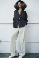 Camisa fluida de corte oversize confeccionada en mezcla de viscosa, con diseño de rayas verticales finas en tono beige sobre fondo blanco. Presenta cuello solapa, cierre frontal con botones, manga larga con puños y un bolsillo de plastrón en el pecho.