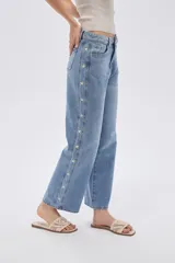 Pantalón de jean azul de corte recto y tiro medio, con detalles de estrellas bordadas a lo largo de los laterales externos de las piernas.