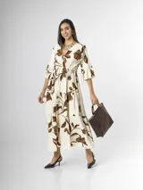 Vestido largo color crudo con estampado floral marrón, escote en V cruzado, mangas tres cuartos con volados y falda con niveles fruncidos.