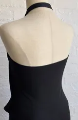 Vestido corto negro con escote halter y detalle de argolla decorativa en el cuello. Presenta un diseño drapeado en la parte superior y falda ajustada.