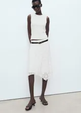 Falda midi de encaje color blanco, tiro medio, con cintura elástica, diseño recto, forro interior y bajo asimétrico con terminaciones en pico.
