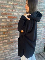 Campera de corderito color verde oscuro, con diseño holgado, cuello alto y manga larga. Presenta una etiqueta de cuero sintético en la manga.