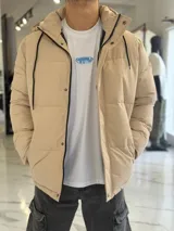Campera puffer impermeable color beige con capucha desmontable con cordones negros, cierre frontal con cremallera y solapa con botones a presión.