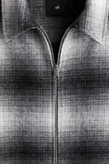 Sobrecamisa de mezcla de lana con acabado cepillado, diseño a cuadros en tonos grises y negros, cuello inglés, cierre frontal bidireccional y bolsillos laterales discretos.