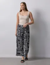 Pantalón ancho estilo palazzo, de seda fría plisada con estampado geométrico en negro, blanco y beige. Tiene pretina ancha elastizada y largo crop.