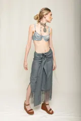 Falda midi color beige de tiro alto y silueta envolvente, con lazo ancho para anudar en la cintura, diseño asimétrico y terminación de flecos largos en el ruedo.