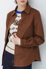 Camisa de estilo casual confeccionada en material tipo gamuza color marrón, con cuello clásico, cierre frontal con botones y costuras a la vista en tono contrastante.