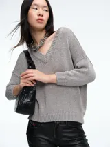 Sweater de punto con brillo, de corte relajado y escote en V. Presenta hombros caídos y mangas largas con puños acanalados.