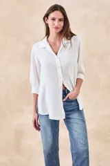 Camisa de corte holgado y fluido, color blanco, con cuello clásico, cierre frontal de botones y mangas tres cuartos con puños rectos.