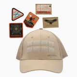 Gorra tipo trucker color beige con paneles frontales de tela y malla trasera. Incluye dos tiras de velcro en la parte frontal para personalizar con parches y logo de la marca estampado en el lateral. Viene con cinco parches intercambiables con diseños de aventura.