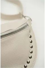 Cartera tipo riñonera o bandolera de cuero sintético negro con textura granulada, forma de media luna y detalles de tachas plateadas en el borde inferior. Cuenta con cierre metálico plateado y correa ajustable.