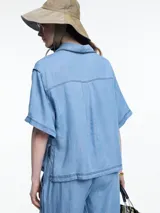 Camisa negra de manga corta confeccionada en denim liviano de tencel, de calce cuadrado y relajado. Presenta cierre frontal con tapeta escondida y costuras en color contraste.