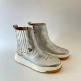 Botas cortas de cuero plateado, con diseño híbrido que combina la estética texana con una suela chunky blanca y detalle de arte lateral creado por Carolina De Cunto.