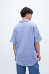 Camisa de manga corta color celeste claro, con cuello solapa clásico y bolsillo en el pecho. Presenta una textura ligera y un calce regular.