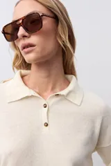 Sweater de punto color crudo, con cuello polo y cierre frontal parcial con botones. Presenta mangas largas y un diseño de calce holgado.